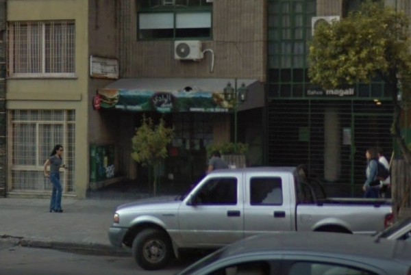 Alwadi: Restaurante con fachada verde y azul, camioneta plateada estacionada frente, personas caminando por la acera.