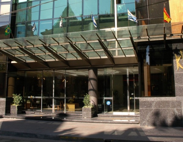 Entrada moderna del King David Flat Hotel con fachada de vidrio y banderas internacionales. Diseño urbano elegante.