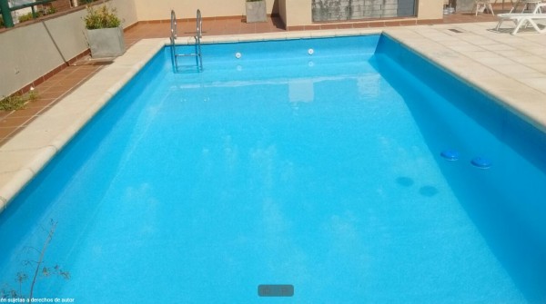 Piscina azul cristalina del Hotel Castelar con escalera metálica y tumbonas blancas alrededor. Ambiente relajante y soleado.
