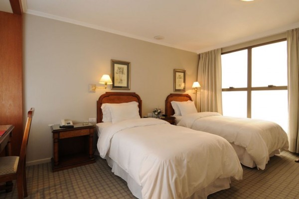 Habitación del Windsor Hotel & Tower con dos camas individuales, mesita de noche y gran ventana iluminada.