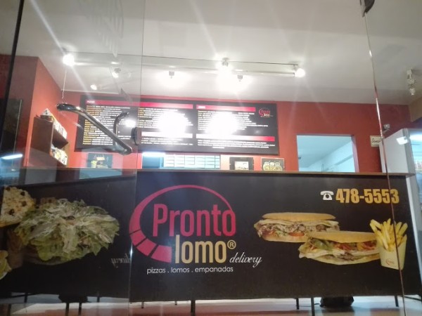 Restaurante Pronto Lomo con menú, pizzas, empanadas y teléfono visible en la ventana. Interior rojo y blanco.
