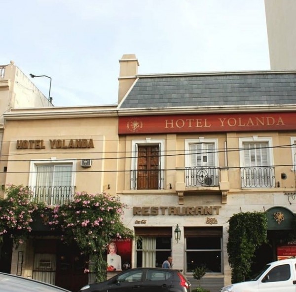 Hotel Yolanda: fachada beige con techo negro, ventanales blancos y letrero rojo. Restaurante en planta baja. Ambiente urbano.