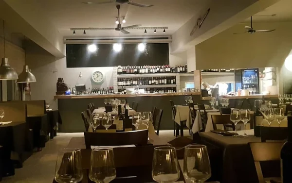 Interior de un restaurante con mesas servidas, barra de vinos y ambiente cálido.