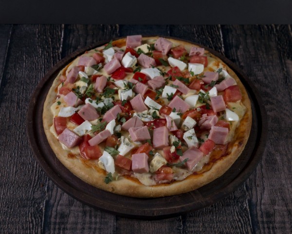 Pizza con jamón, tomate y queso en Pizzería La Juana. Plato apetitoso sobre mesa de madera oscura.