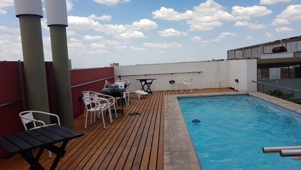 Terraza del King David Flat Hotel con piscina azul, mesas negras y sillas blancas bajo cielo nublado.
