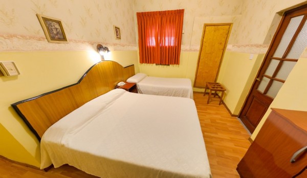 Habitación acogedora del Gran Savoy con dos camas, cortinas rojas y decoración clásica en tonos amarillos y marrones.