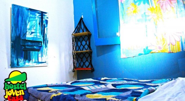 Habitación acogedora con paredes azules, cama colorida, cuadro abstracto y estante de madera. Hostel Joven.