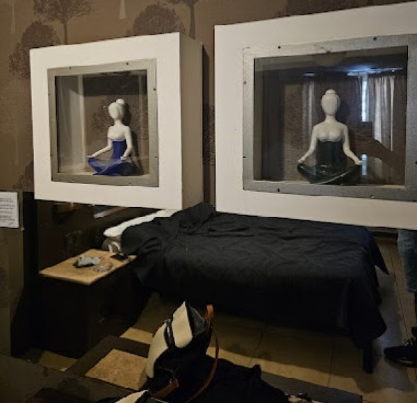 Dos maniquíes sentados en cuadros, una mesa con tela negra y objetos sobre el piso.