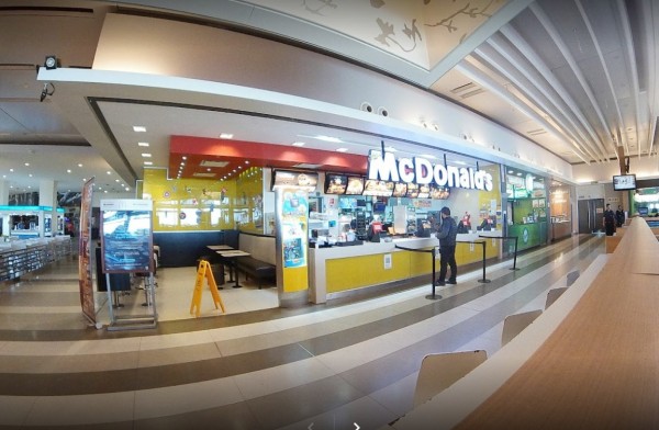 Interior de McDonald's con mostrador amarillo, mesas vacías y cliente en fila. Iluminación brillante y ambiente limpio.