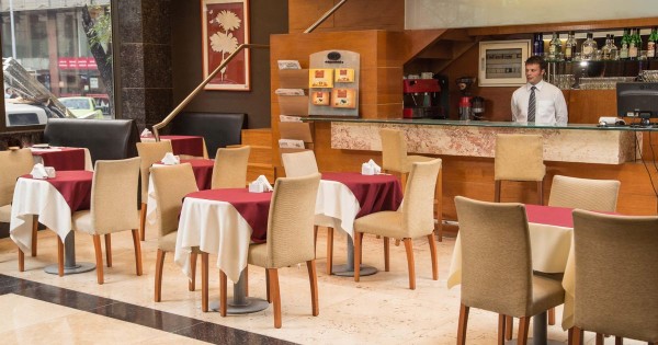 Restaurante del King David Flat Hotel con mesas rojas y blancas, sillas beige y barra de madera. Ambiente acogedor.
