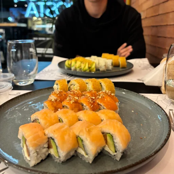 Platos de makis y rolls de salmón sobre la mesa en un restaurante de sushi con paredes de ladrillo.