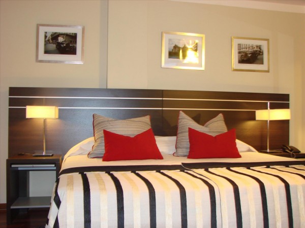 Habitación moderna de Zoom Apartments con cama grande, almohadas rojas y negras, lámparas y fotos en la pared.
