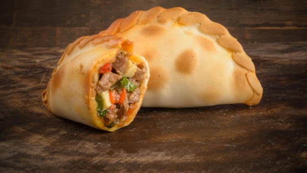 Empanada dorada de El Hornito Santiagueño, rellena con carne, verduras y queso, sobre superficie madera rústica.
