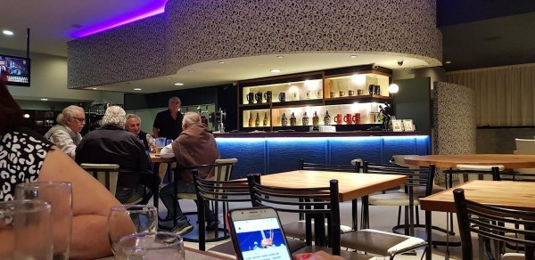 Interior moderno de Punto Urca con bar azul, mesas de madera y personas disfrutando bebidas. Ambiente acogedor y elegante.