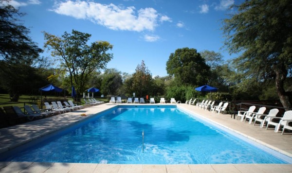 Piscina azul en Howard Johnson rodeada de árboles y sillas blancas bajo un cielo despejado.
