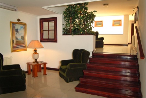 Hotel Castelar: Hall con escaleras rojas, sillones verdes, lámpara y cuadros decorativos. Ambiente acogedor y elegante.