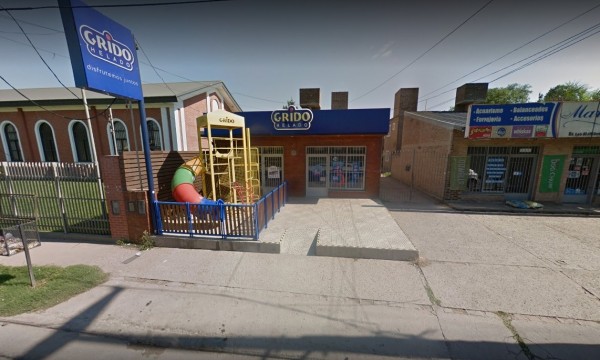 Entrada de Grido con parque infantil, edificio de ladrillo y letrero azul destacado en la calle.
