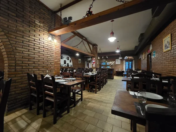 Interior de un restaurante con mesas de madera, paredes de ladrillo y iluminación cálida.