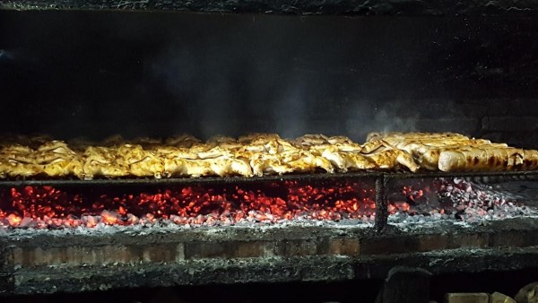 Asado en La Rueda: carnes doradas sobre brasas rojas, humo ascendente, ambiente cálido y acogedor.