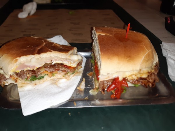 Hamburguesa grande cortada por la mitad, con carne, queso y vegetales, servida en bandeja metálica.