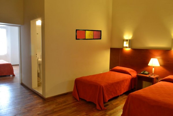 Habitación acogedora del Gran Hotel Victoria con camas rojas, lámparas y cuadro colorido en la pared.