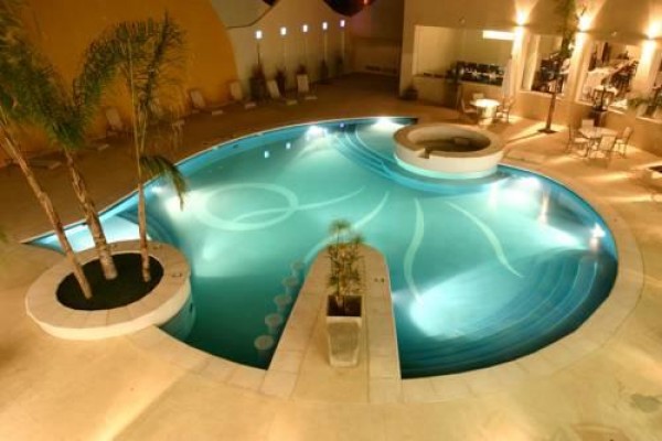 Piscina iluminada con diseño circular en Quorum Hotel & Spa, rodeada de palmeras y mobiliario elegante.