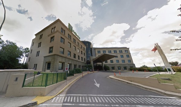 Hotel Holiday Inn Córdoba: edificio moderno con entrada principal, banderas y camino de acceso. Cielo nublado.