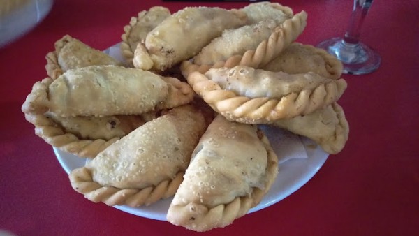 Empanadas doradas y crujientes en plato blanco sobre mesa roja, junto a pie de copa de vino.