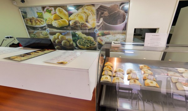 Vitrina con empanadas y cartelera de comidas variadas en fondo. Ambiente de cafetería o panadería.