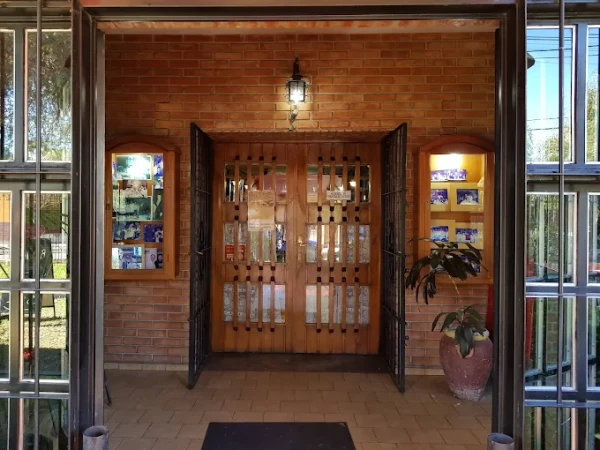 Entrada de local con puertas de madera y vidrios, paredes de ladrillo, mostradores laterales y planta decorativa.