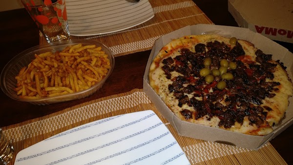 Pizza con aceitunas y champiñones en caja de Pizzería Moma, acompañada de papas fritas en mesa rústica.
