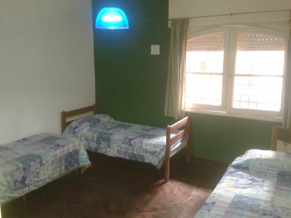 Habitación RUNC con tres camas individuales, pared verde, ventana grande y lámpara azul en el techo.