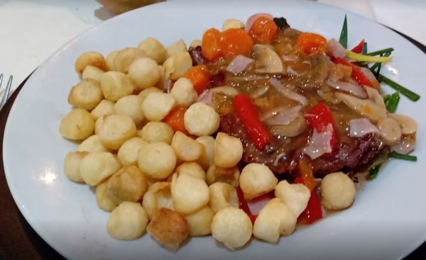 Plato de carne con salsa acompañado de croquetas y verduras en un restaurante