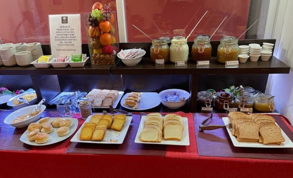 Mesa con panes, mermeladas, frutas y dulces dispuestos para un desayuno o merienda.