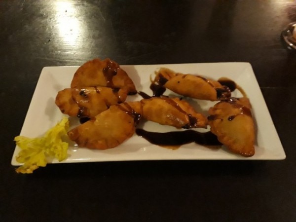 Empanadas doradas con salsa oscura y adorno amarillo en plato blanco sobre mesa negra en Palito Rojo.